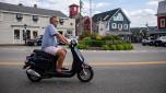 A man rides a Wolf Lucky scooter through the streets in Kennebunkport, Maine on July 22, 2022. - Weather in New England reached into the 90s (F) today and forecast call for temperatures to be close to 100 degrees (F) over the weekend. (Photo by Joseph Prezioso / AFP)