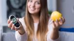 Young diabetic woman holding glucometer and apple
