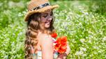 Happy small girl with beauty look wear sun hat on long curly blonde hair holding poppy flowers on natural sunny summer landscape, salon.