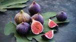 Whole and sliced figs on big fig leaves. Fresh ripe sweet fruits on dark background. Close-up. Selective focus. Blurred background.