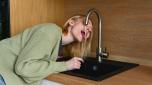 Woman drinking water from kitchen faucet