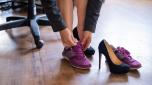 A business woman exchanges high heels for comfortable shoes in the workplace. A close-up of female hands takes off her black shoes and puts on colored sneakers in the office after a long working day