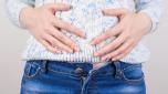 Cropped closeup photo of girl suffering from painful symptoms in abdomen holding hands on big round tummy isolated grey background