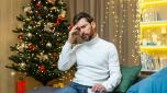 A sick man with a cold sits on the sofa for Christmas, celebrates the New Year and Christmas holidays, holds his head with a napkin in his hands.