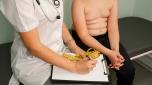 Fat boy at a nutritionist appointment. Overweight boy consulting with doctor in office. Childhood obesity problem and weight loss. Doctor examining fat boy in clinic. Doctor measuring overweight boy.