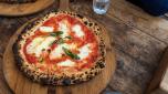 Margherita Italian pizza on the thin base with melted mozzarella cheese and tomato, garnished with basil, crispy crust