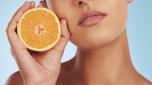Woman, hands and orange for vitamin C, skincare or diet against a blue studio background. Closeup of female person holding organic citrus fruit for natural nutrition, dermatology or healthy wellness