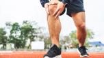 Young man runner has sore knee because he ran too long. Male Exercising until the injury. Overtrained. Young sport man accident running on track