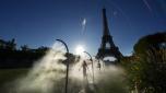 A spectator walks through a water mist sprayer on her way to the Eiffel Tower Stadium to watch a beach volleyball match at the 2024 Summer Olympics, Sunday, July 28, 2024, in Paris, France. (AP Photo/Robert F. Bukaty)