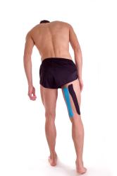 Athlete standing on white background, Hamstring taped with kinesiology tape. Rear viewpoint