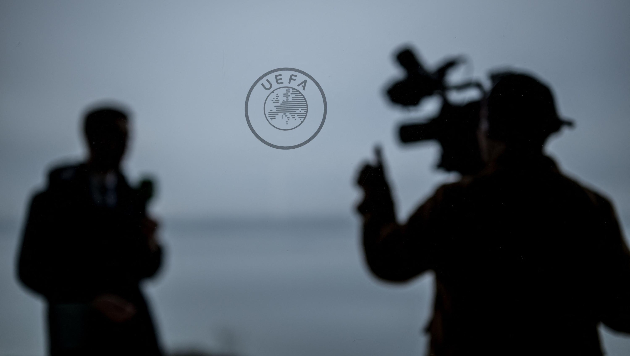 A tv crew operates next to a sign of the UEFA at the House of European Football in Nyon, on December 18, 2023. (Photo by Fabrice COFFRINI / AFP)