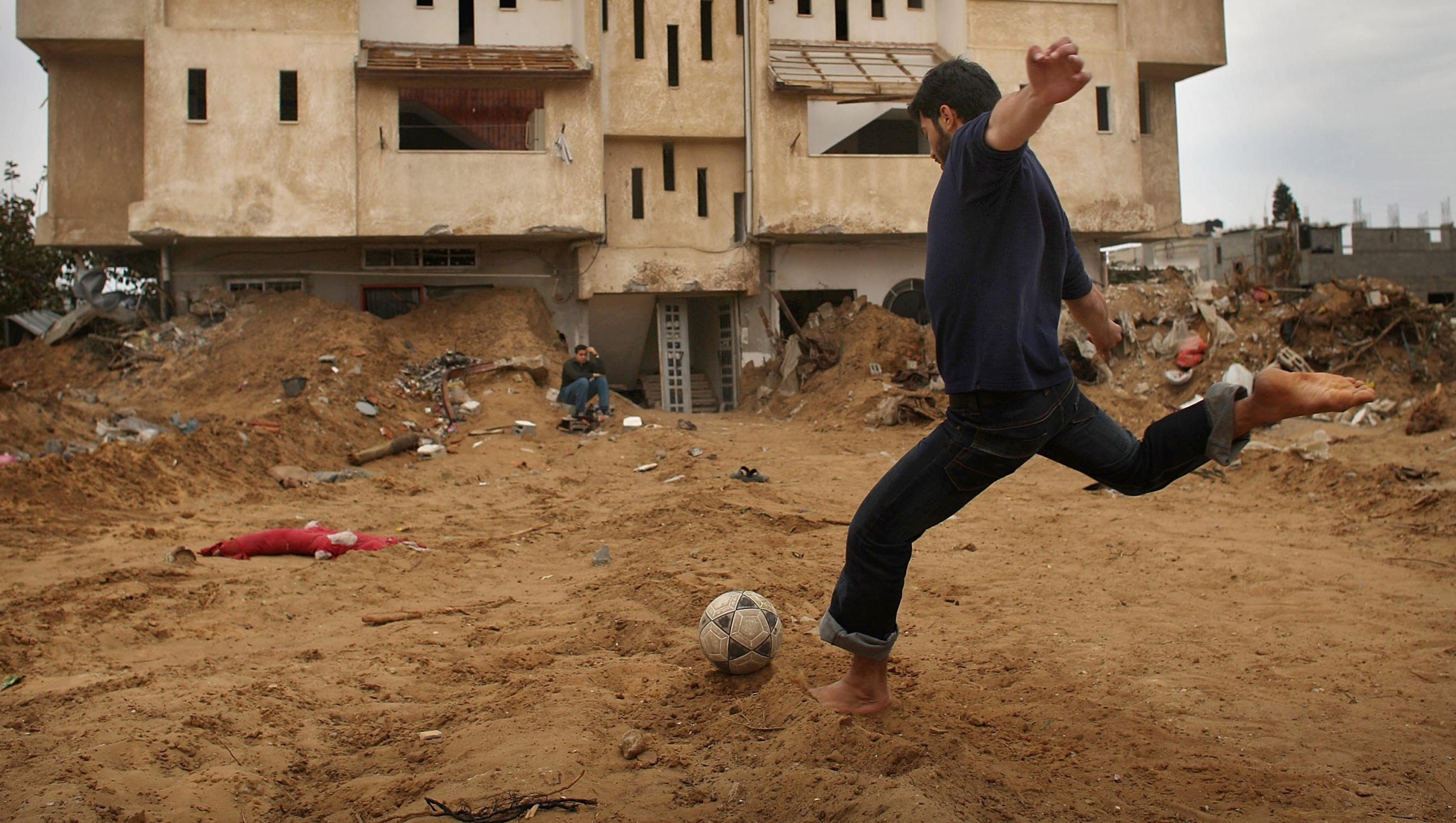 GAZA CITY, GAZA STRIP - JANUARY 23:  A teenager plays a game of soccer with friends in front of his damaged apartment building on January 23, 2009 in a heavily damaged suburb in Gaza City, Gaza Strip. Residents of Gaza are still suffering from severe food and water shortages. According to reports, 13 Israelis and over 1300 Palestinians were killed in the Mideast conflict.  (Photo by Spencer Platt/Getty Images)