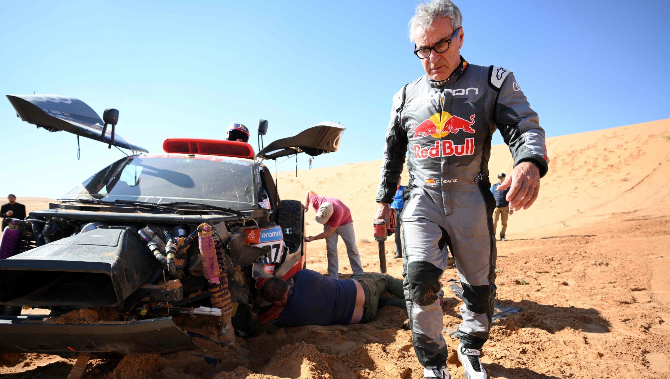 Audi's hybrid driver Carlos Sainz (R) of Spain walks next to his car after a crash during the Stage 6 of the Dakar 2023 between Ha'il and Al Duwadimi, Saudi Arabia, on January 6, 2023. (Photo by FRANCK FIFE / AFP)