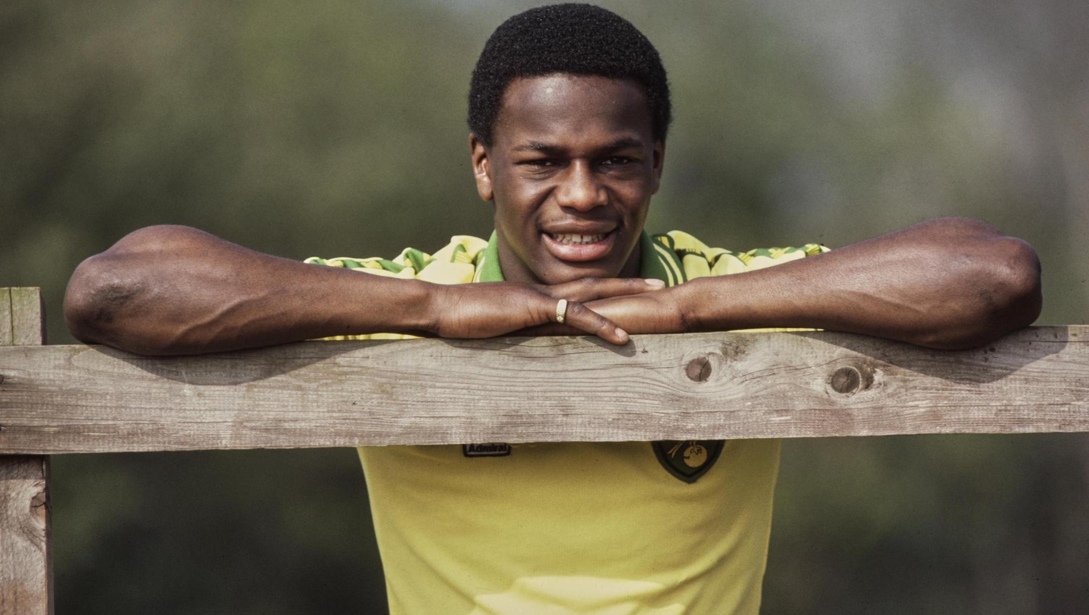 British footballer Justin Fashanu, wearing a Norwich City shirt, leans with both arms and his head resting on the wooden rail of a fence, United Kingdom, circa 1980. (Photo by Allsport/Hulton Archive/Getty Images)