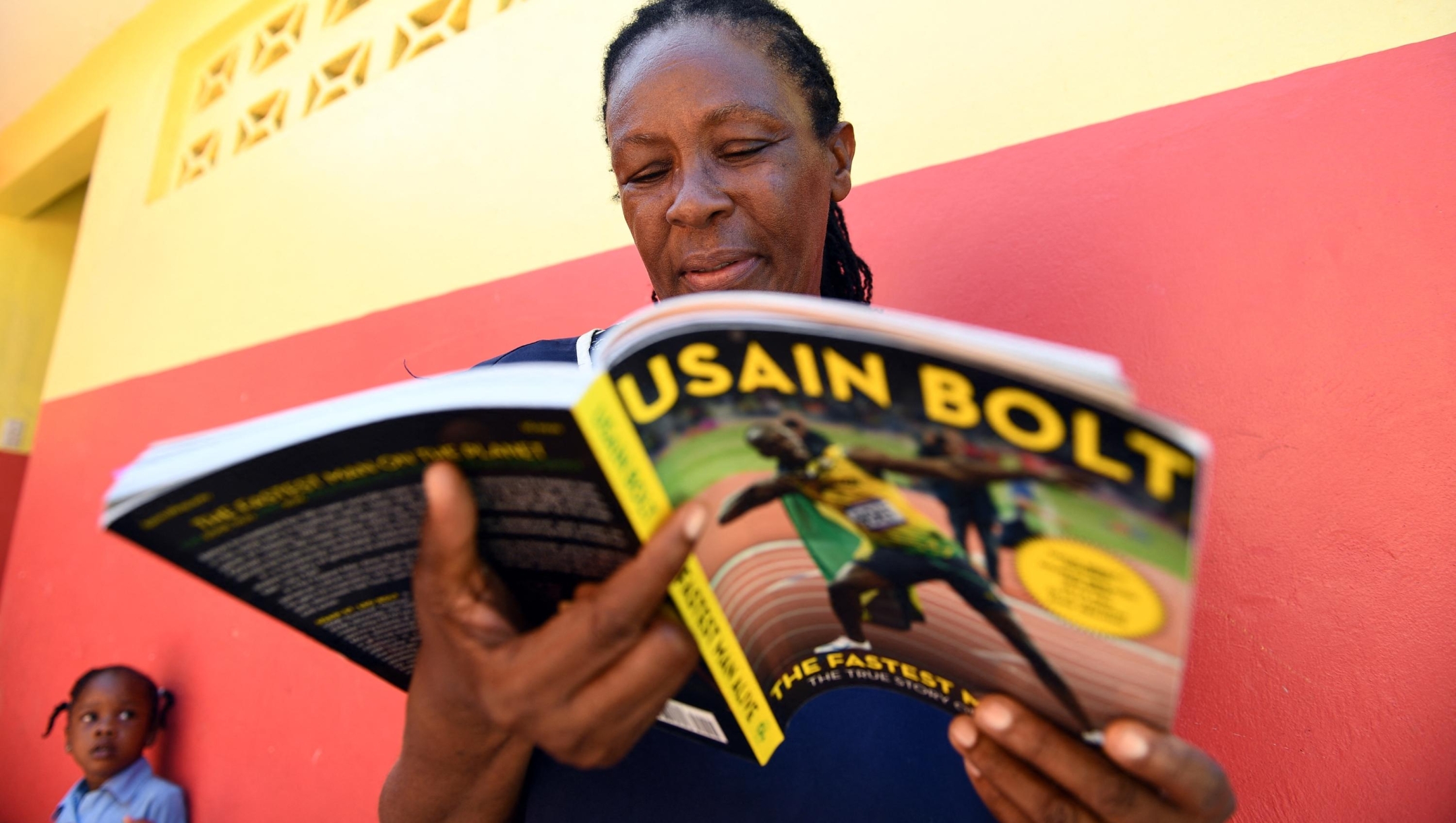 Jamaican sprinter Usain Bolt's elementary teacher Sheron Seivwright reads a book about him during a break at the Waldensia elementary school in Sherwood Content on June 7, 2017. Usain Bolt, the greatest sprinter in history with eight Olympic golds, 11 world titles and three world records, will retire from international competition after the IAAF world championships in August. (Photo by Jewel SAMAD / AFP)