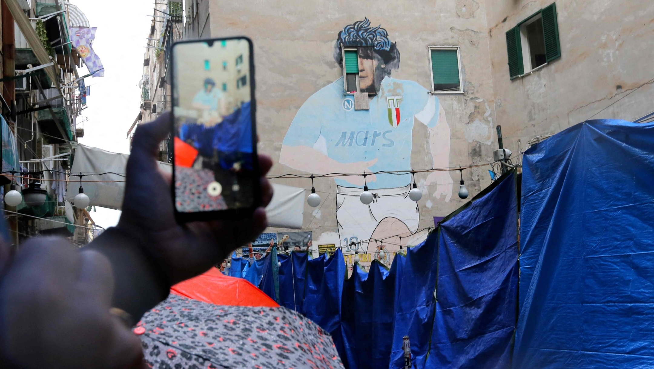 Blue tarps close the access to Largo Maradona in the Spanish quarters of Naples on October 16, 2025. The Largo Maradona hosting the famous murales dipicting Argentinian football legend Diego Armando Maradona was closed two days ago by people managing the former parking area and owners of bars to protest against a blitz by the municipality of Naples who investigates the commercial activities of the area and seized unlicensed merchandising. (Photo by Carlo Hermann / AFP)