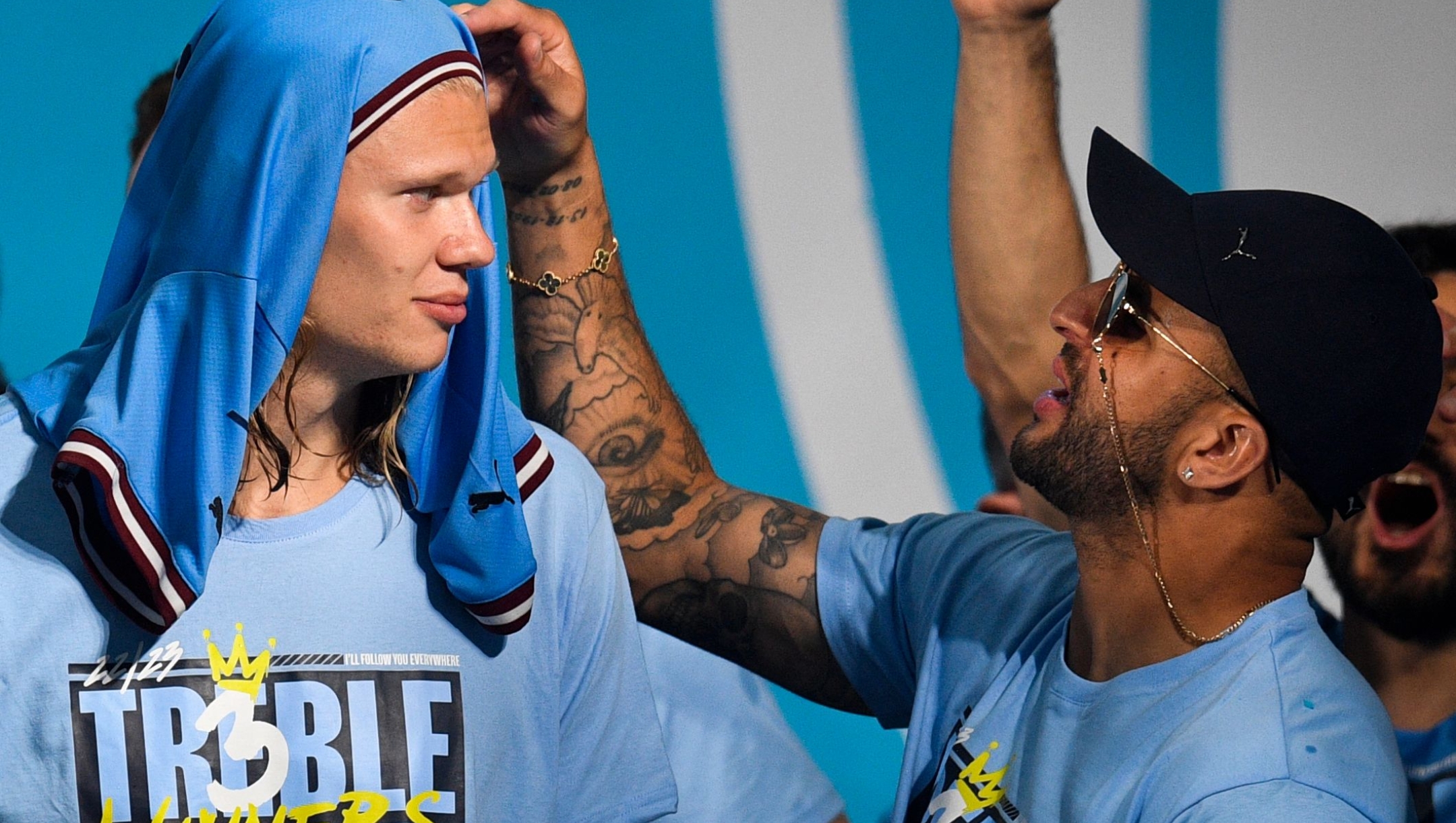 Manchester City's English defender Kyle Walker (R) plays with Manchester City's Norwegian striker Erling Haaland 's hairs as they celebrate on stage following an open-top bus victory parade for their European Cup, FA Cup and Premier League victories, in Manchester, northern England on June 12, 2023. Manchester City tasted Champions League glory at last on Saturday as a second-half Rodri strike gave the favourites a 1-0 victory over Inter Milan in a tense final, allowing Pep Guardiola's side to complete a remarkable treble. Having already claimed a fifth Premier League title in six seasons, and added the FA Cup, City are the first English club to win such a treble since Manchester United in 1999. (Photo by Oli SCARFF / AFP)