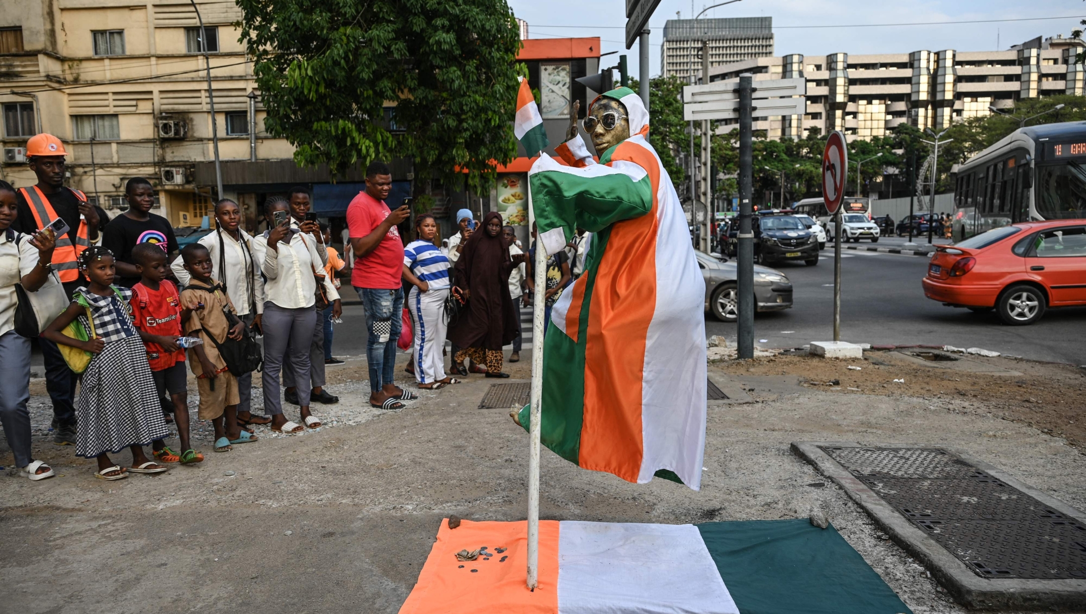 TOPSHOT - A man dressed in national colors sitting on a support poses for a photo on the eve of the start of 2024 Africa Cup of Nations (CAN) football tournament, at the Plateau in the business district of Abidjan on January 12, 2024. (Photo by Sia KAMBOU / AFP)
