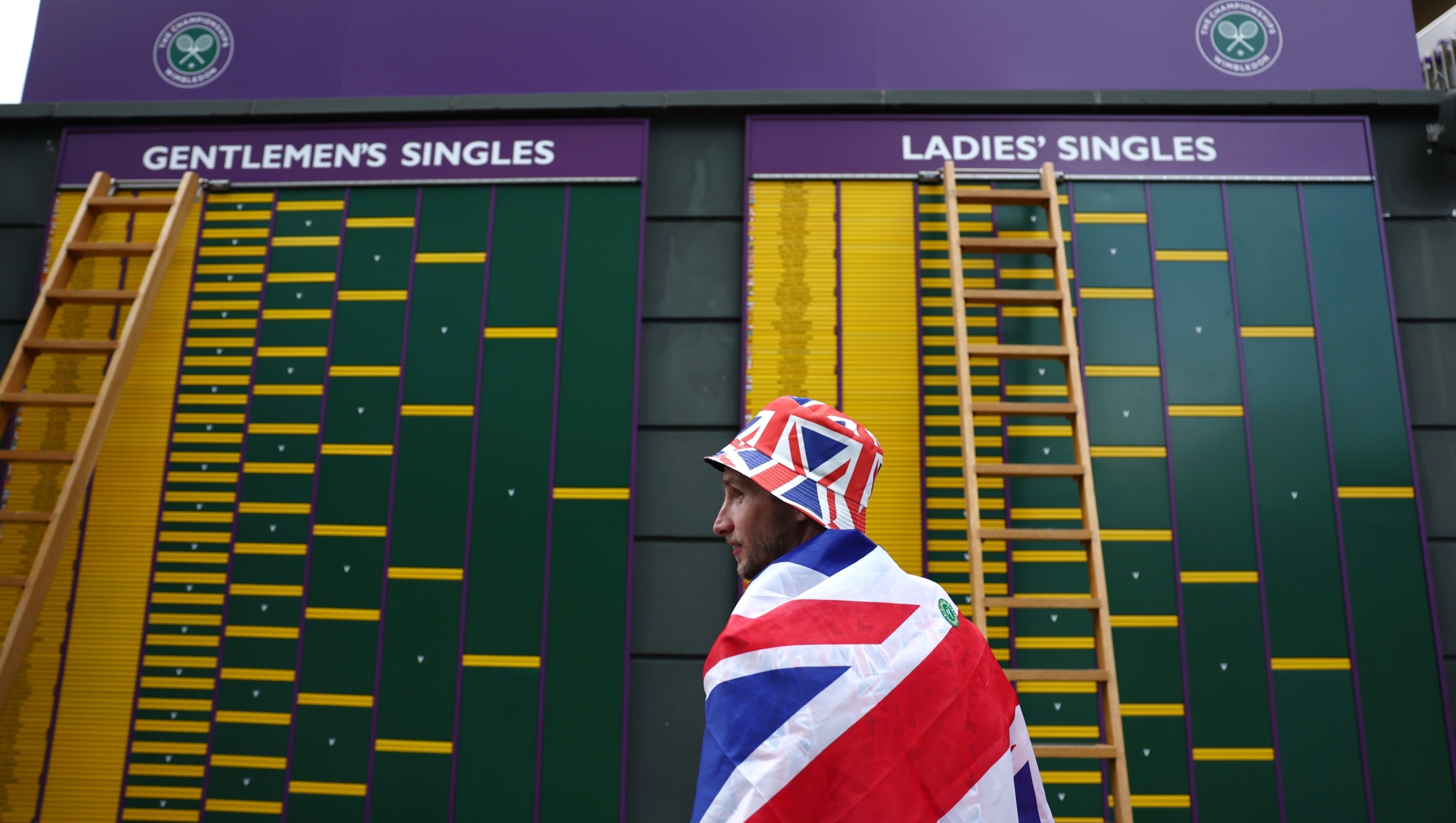 LONDON, ENGLAND - JULY 01: A spectator wearing the Union Flag observes the order of play board during day one of The Championships Wimbledon 2024 at All England Lawn Tennis and Croquet Club on July 01, 2024 in London, England. (Photo by Francois Nel/Getty Images)