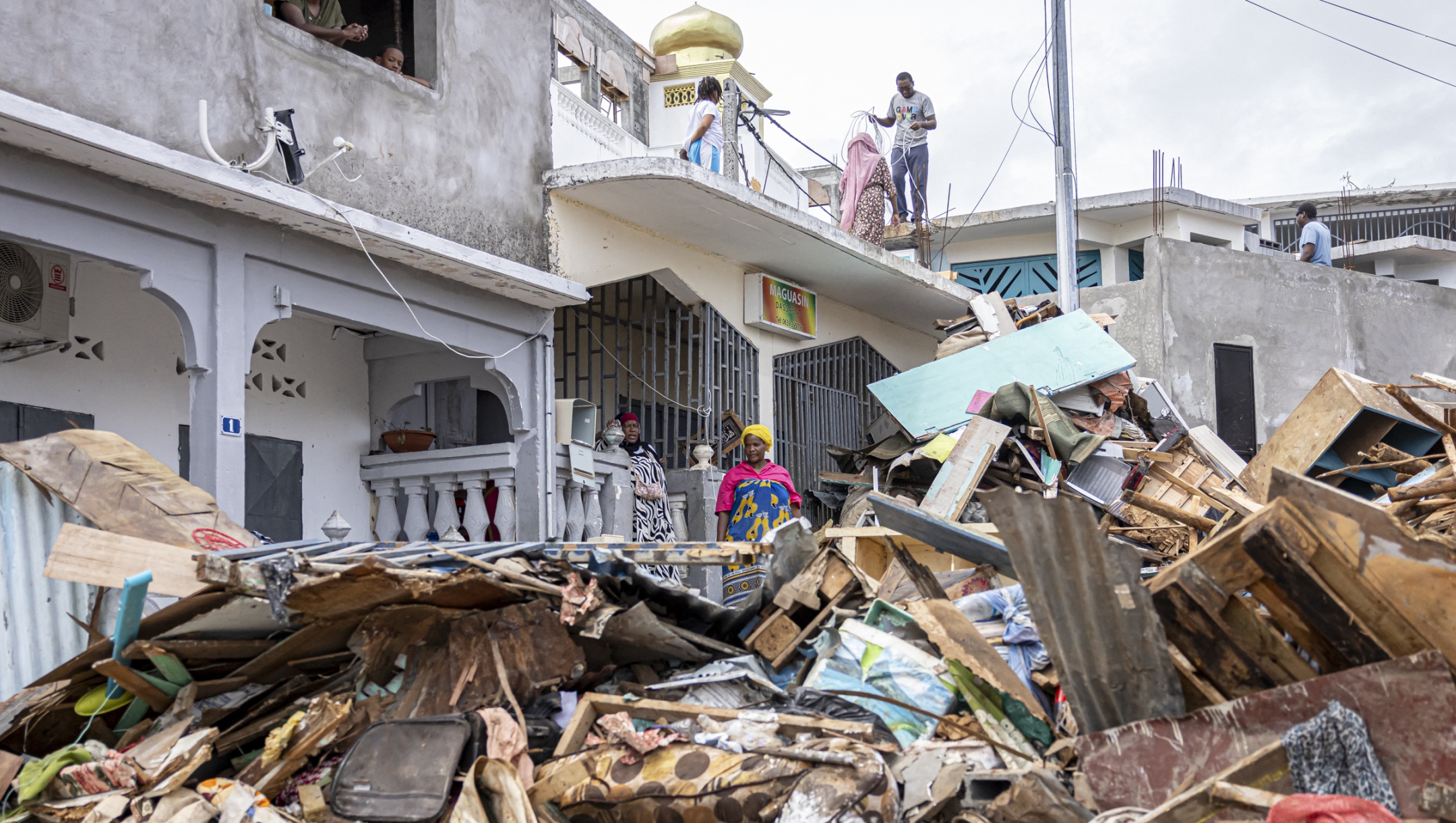 Residents watch as workers clear a street in the city of Mamoudzou on the French Indian Ocean territory of Mayotte, after the cyclone Chido hit the archipelago on December 22, 2024. Paris declared "exceptional natural disaster" measures for Mayotte, France's poorest region near Madagascar off the coast of southeastern Africa. (Photo by PATRICK MEINHARDT / AFP)