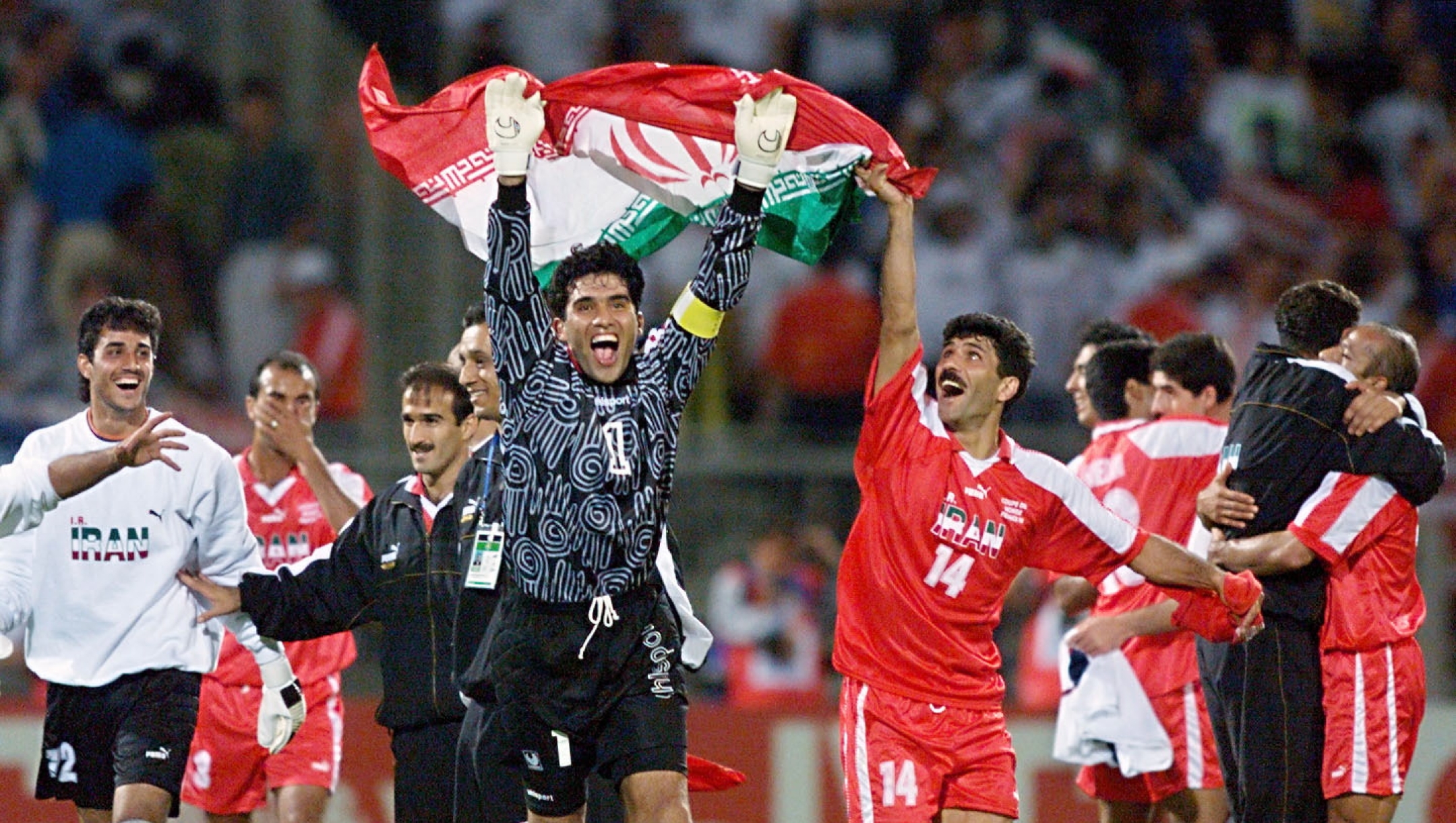 Iranian goalkeeper Ahmad Abedzadeh (C) waves his national flag as he celebrates with Nader Mohammadkhani (14) after winning their 1998 Soccer World Cup Group F first round second match against the United States at the Gerland stadium 21 June in Lyon, central France. Iran won 2-1. (Iranian player L is Mehdi Mahdavikia) (ELECTRONIC IMAGE) AFP PHOTO PATRICK KOVARIK (Photo by PATRICK KOVARIK / AFP)