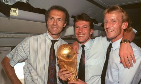 FILED - 09 July 1990, Italy, Rom: On the plane returning from Rome to Frankfurt, former DFB team manager Franz Beckenbauer (l), captain and midfielder Lothar Matthäus (M) and defender Andreas Brehme, who scored the decisive goal, present the World Cup trophy. Franz Beckenbauer is dead. The German soccer legend died on Sunday at the age of 78, his family told the German Press Agency on Monday. Photo: Wolfgang Eilmes/dpa (Photo by WOLFGANG EILMES / DPA / dpa Picture-Alliance via AFP)