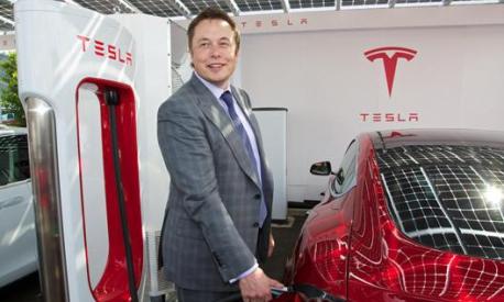 Elon Musk e sullo sfondo l’originale logo di Tesla