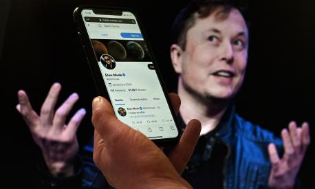 (FILES) In this file photo illustration, a phone screen displays the Twitter account of Elon Musk with a photo of him shown in the background, on April 14, 2022, in Washington, DC. - Twitter shares slid late on July 7, 2022 after a Washington Post report that Elon Musk's $44 billion deal to buy the social media giant is in danger. (Photo by Olivier DOULIERY / AFP)