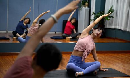 This photo taken on July 30, 2022 shows yoga instructor Feng (R) stretching with students at a gym in Beijing's middle-class neighbourhood of Shangdi. - It is 10 years since Xi unveiled the "Chinese Dream", a grand vision to restore the country's global influence through a collective struggle for prosperity, power and glory, steered by the Chinese Communist Party. (Photo by NOEL CELIS / AFP) / TO GO WITH China-Xi-congress-economy-politics, SPECIAL REPORT by Matthew WALSH