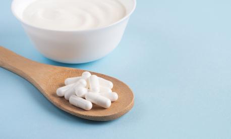 Homemade yogurt with probiotics and capsules pills on a wooden spoon. Close up, copy space
