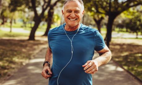 Portrait of a senior man in fitness wear running in a park. Close up of a smiling man running while listening to music using earphones.