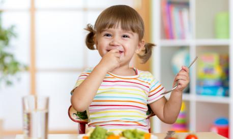 Funny kid girl eating healthy food in kindergarten