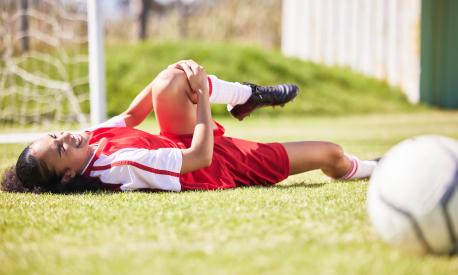 injured, pain or injury of a female soccer player lying on a field holding her knee during a match. Hurt woman footballer  with a painful leg on the ground in agony having a bad day on the pitch