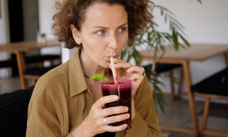 A young Caucasian woman enjoys her healthy organic cold pressed beetroot juice. Sipping it through the paper straw in a tropical cafe.Useful detox food from fresh fruits.