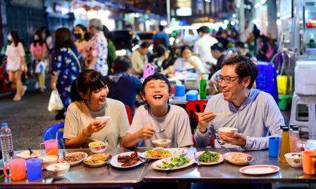 Asian family enjoy eating food on street food restaurant with crowd of people at Yaowarat road, Bangkok