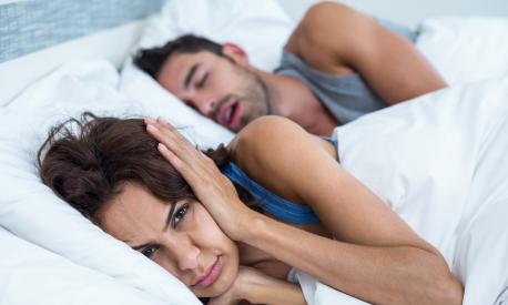 Portrait of woman blocking ears with hands while man snoring on bed