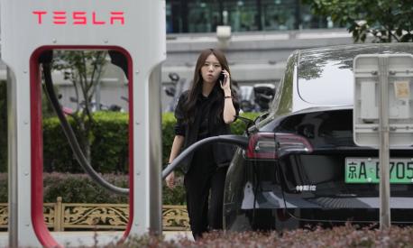 A worker stands next to a Tesla being charged in Beijing, Tuesday, May 30, 2023. China?s foreign minister met Tesla Ltd. CEO Elon Musk on Tuesday and said strained U.S.-Chinese relations require ?mutual respect,? while delivering a message of reassurance that foreign companies are welcome. (AP Photo/Ng Han Guan)