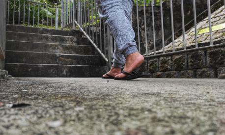 Female feet in long pants and black flip flops stepped on the concrete floor towards the stairs with an iron fence.