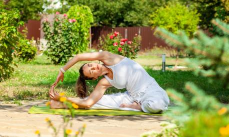 Young woman practices yoga in the summer garden - Inverted tilt of the head to the knee, parivritta Janu Shirshasana.