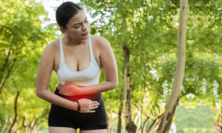 Woman in sportswear with stomach ache in a park. Running woman with digestive problems. Sport girl with stomach ache outdoors with copy space. Fatigued young woman with stomach ache