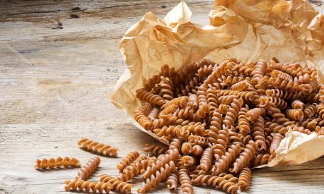 wholemeal pasta fusilli from organic whole grain spelt falling from a paper bag on a rustic wooden table, copy space