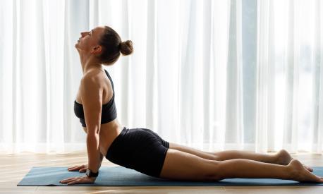 Young woman doing yoga vinyasa flow against big window with white curtains in the morning.