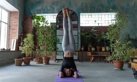 Slim woman doing headstand, posing Sirsasana Yoga type Arm balance. Girl fitness in loft apartments with potted house plants. V