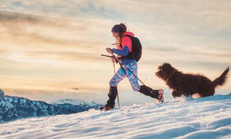 Sporty girl with her dog during an alpine trekking on the snow