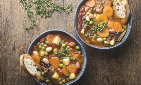 Minestrone vegetable soup on a wooden textured background with pieces of toasted bread and herbs. Simple vegan rustic Italian dish, classic of Italian cuisine, delicious healthy Mediterranean lunch