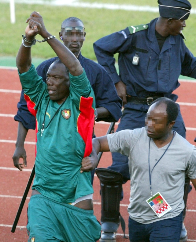 Thomas N'kono, (L) the assistant to Cameroon's German trainer Winfried Schaefer holds up his handcuffed hands 07 February 2002 in Bamako after about a dozen Malian policemen arrested him on the edge of the pitch about an hour and a half before Cameroon was to play Mali in their African Nations Cup semi-final match. A policeman held up an object to the crowd after the arrest and according to certain Malian witnesses, the police suspected the assistant, N'kono of having thrown a gri-gri (magical item) onto the pitch.  AFP PHOTO STR