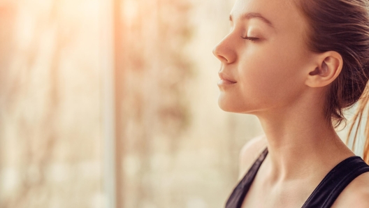 Side view of young female with closed eyes breathing deeply while doing respiration exercise during yoga session in gym