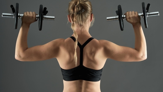 Young fit woman with dumbbells doing shoulder workout