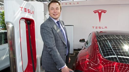 Elon Musk e sullo sfondo l’originale logo di Tesla