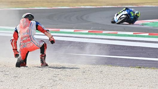 Bagnaia dopo la caduta, mentre sfreccia Mir. Afp